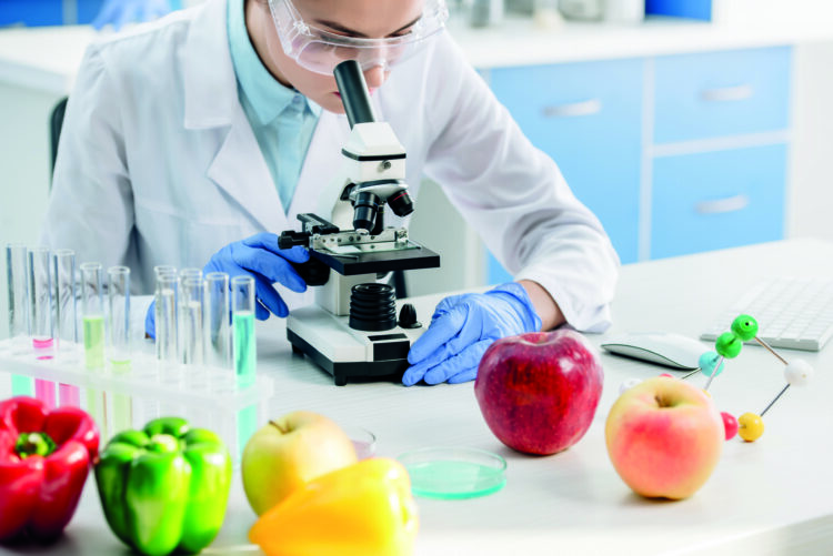 cropped view of molecular nutritionist using microscope and sitting at table