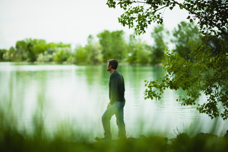A man standing alone looking into the distance across the water, deep in thought.